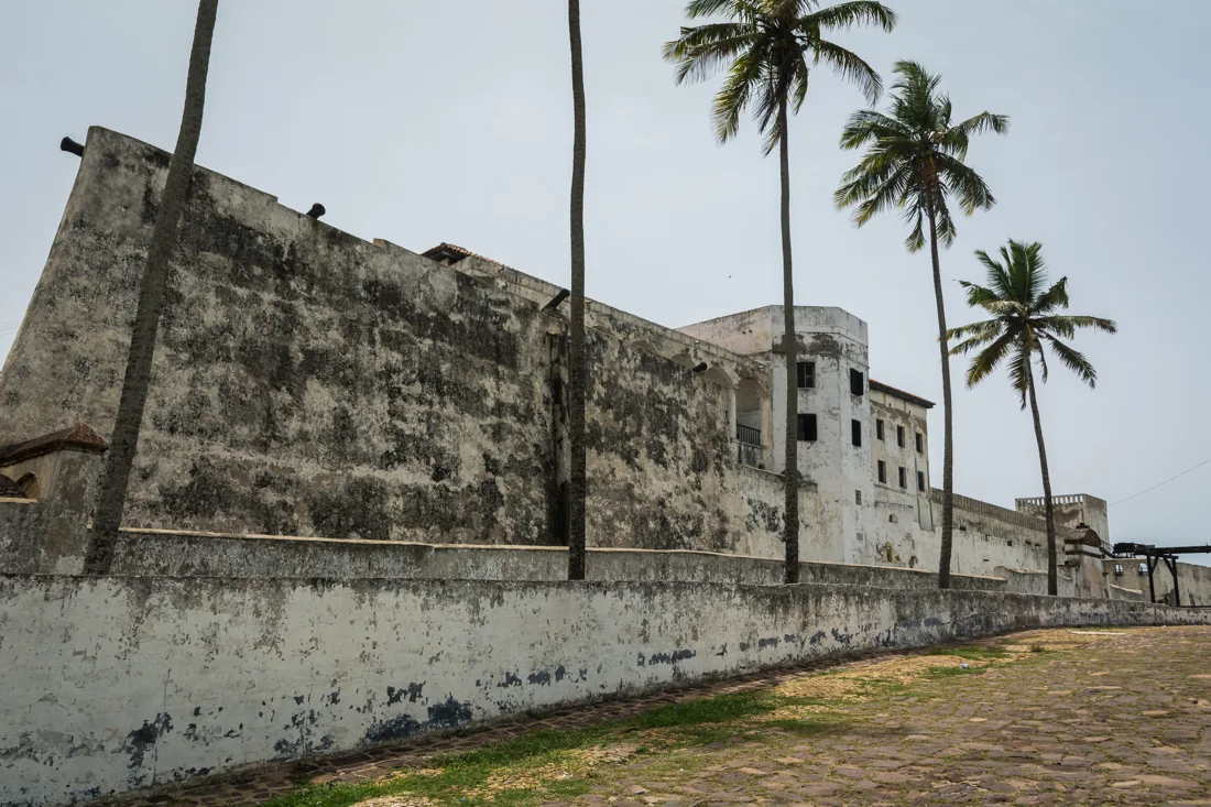 Historic walls of Elmina Castle framed by palms